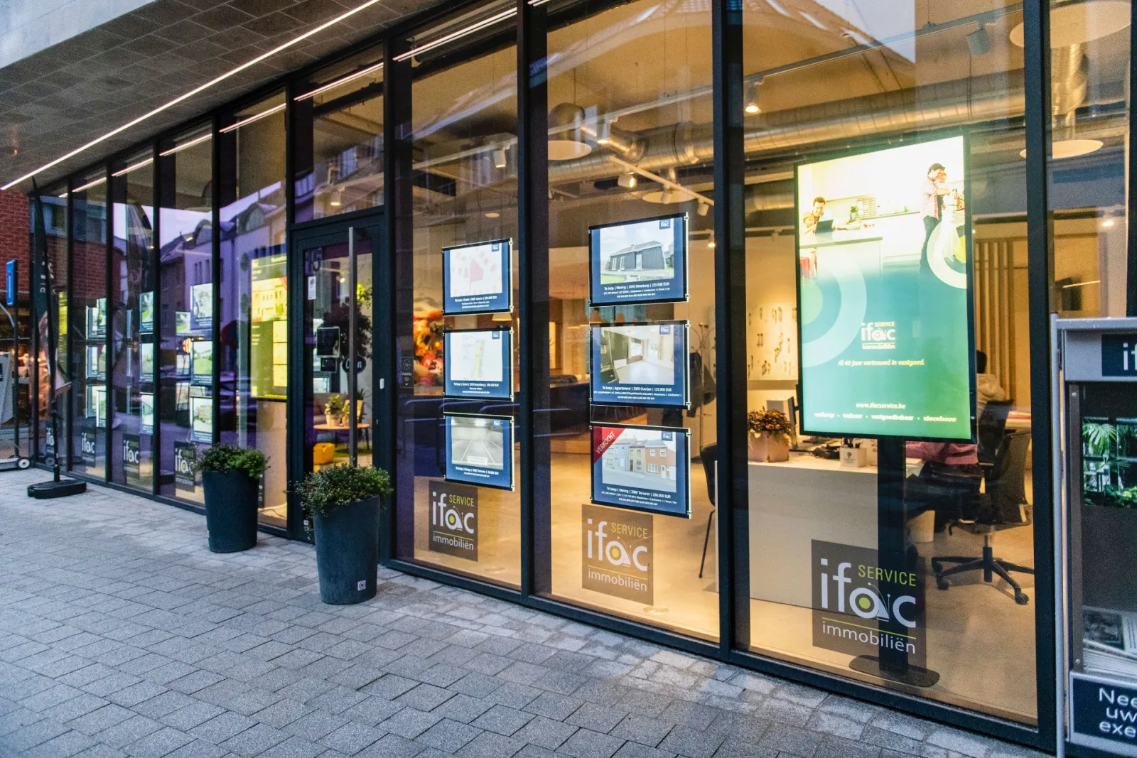 La vitrine d'Ifac Service le soir, avec un écran en portrait et des biens éclairés