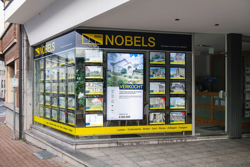 L'agence d'angle d'Immo Nobels, avec un écran et des biens éclairés en vitrine