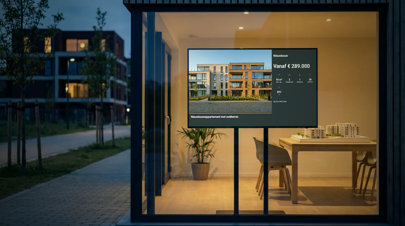 Glass sales pavilion at a new development at dusk, with a screen on a stand showing a new-build flat from 289,000 euros and a scale model on the table